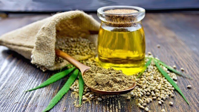 Flour hemp in a wooden spoon, hemp seed in a bag and on the table, hemp oil in a glass jar, hemp leaves on the background of wooden boards