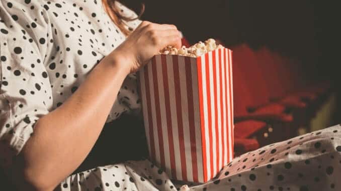 Frau mit Kleid sitzt im Kino und isst veganes Popcorn